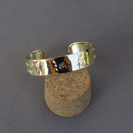 Bracelet laiton symbole OM avec gravure centrale OM et motifs spirales, fabriqué artisanalement en atelier breton. Bracelet ajustable avec texture martelée et finition brillante, inspiré des traditions spirituelles.