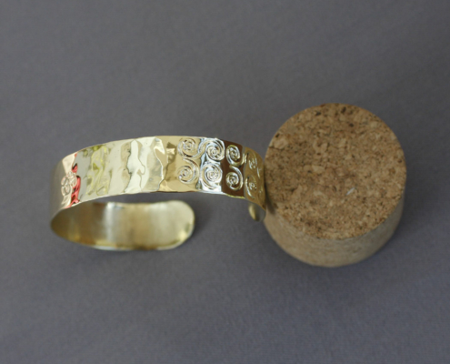 Bracelet laiton martelé symbole avec motifs spirales et OM, fabriqué artisanalement en atelier breton. Texture martelée avec gravures inspirées des traditions spirituelles, bracelet ajustable avec finition brillante.