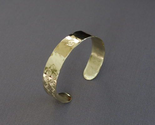 Bracelet laiton martelé symbole avec motifs spirale et OM, fabriqué à la main en atelier breton. Finition brillante et texture martelée, bracelet ajustable avec gravures symboliques inspirées des traditions spirituelles.