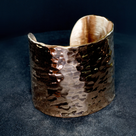 Bracelet manchette en cuivre large martelé, posé sur un fond sombre en velours.