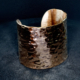 Bracelet manchette en cuivre large martelé, posé sur un fond sombre en velours.