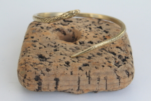 Bracelet ouvert en laiton en forme de serpent, sculpté et texturé, présenté sur un support en liège.