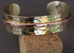 Bracelet artisanal en laiton martelé et cuivre, modèle mixte riveté, posé sur un support en liège.