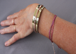 Bracelet cuivre et laiton martelé riveté porté au poignet, bijou artisanal mixte sur fond gris.
