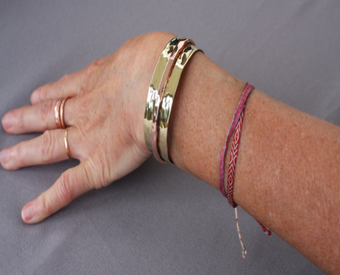 bracelets-cuivre-laiton-martele-poiconne-arthrose-mixte-clmduorivet-4-porte.jpg Bracelet cuivre et laiton martelé riveté porté au poignet, bijou artisanal mixte sur fond gris.