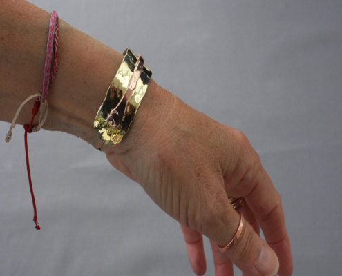 bracelets-cuivre-laiton-martele-poiconne-arthrose-mixte-clmduorivet-5-porte.jpg Bracelet cuivre et laiton martelé riveté vu de profil, porté au poignet, bijou artisanal fait main.