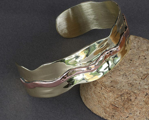 bracelets-cuivre-laiton-martele-poiconne-arthrose-mixte-clmduorivet-5.jpg Bracelet martelé en laiton et cuivre ondulé, vue en diagonale, bijou artisanal aux reflets brillants.