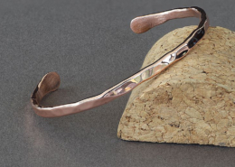 Bracelet jonc en cuivre martelé, fabriqué à la main à partir d’un fil de 3 mm, posé sur un support en liège. La surface brillante et irrégulière reflète la lumière, mettant en valeur le travail artisanal du métal.