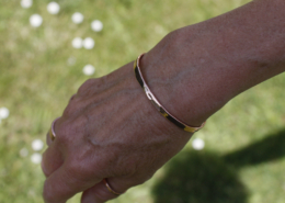Bracelet jonc en cuivre martelé porté au poignet d’une femme, en extérieur sur fond d’herbe verte, mettant en valeur l’éclat du métal au soleil.