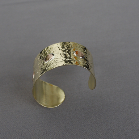 Bracelet laiton martelé riveté cuivre, large et ajustable, avec texture martelée artisanale et trois rivets en cuivre rouge, photographié sur fond gris. Bijou mixte fait main en Bretagne.