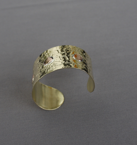 Bracelet laiton martelé riveté cuivre, large et ajustable, avec texture martelée artisanale et trois rivets en cuivre rouge, photographié sur fond gris. Bijou mixte fait main en Bretagne.