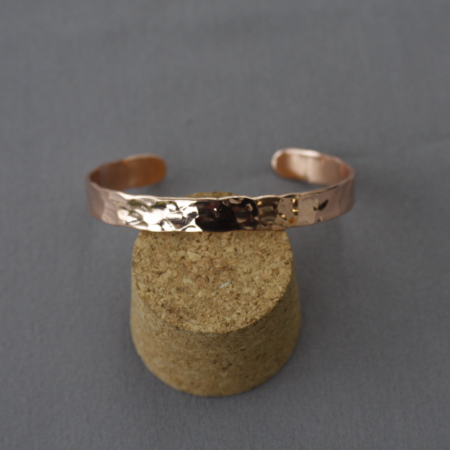Bracelet en cuivre martelé avec facettes irrégulières, posé sur un support en liège, fabrication artisanale Cuivre Island.