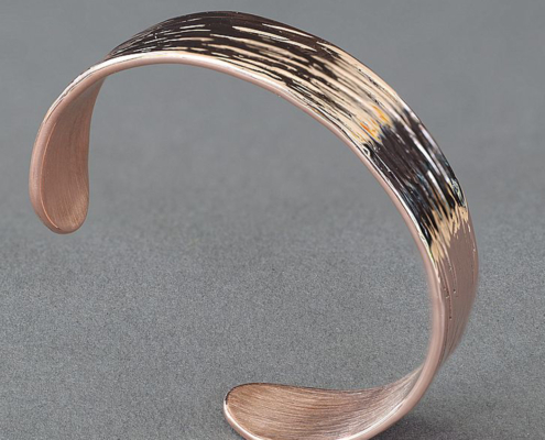 Bracelet en cuivre martelé avec finition striée intense, présenté sur fond gris, vu en perspective.