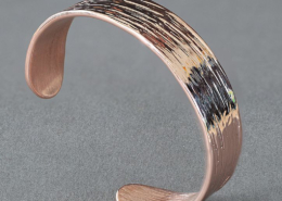 Bracelet en cuivre martelé avec stries profondes, présenté en vue latérale sur fond gris.