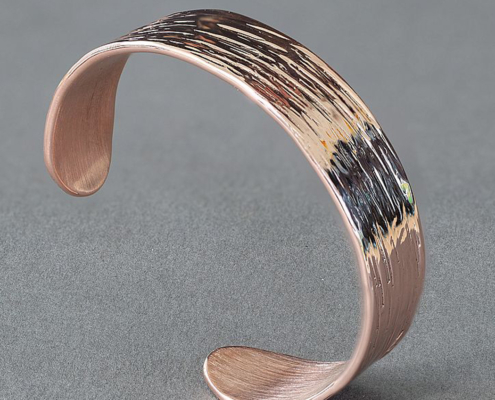 Bracelet en cuivre martelé avec stries profondes, présenté en vue latérale sur fond gris.