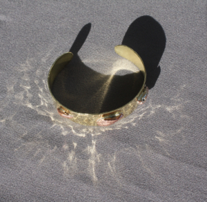 Bracelet laiton cuivre Origine projetant des reflets lumineux sur un tissu gris.