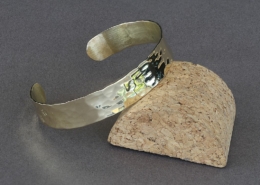 Bracelet en laiton martelé chat avec pattes de chat, posé sur un support en liège, fond gris.