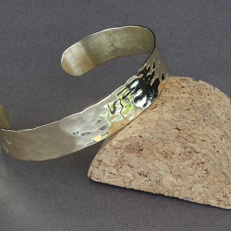 Bracelet en laiton martelé chat avec pattes de chat, posé sur un support en liège, fond gris.