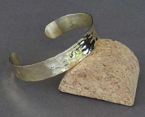 Bracelet en laiton martelé chat avec pattes de chat, posé sur un support en liège, fond gris.