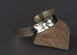 Bracelet laiton martelé chat posé sur support en liège, reflet lumineux sur sa surface brillante.