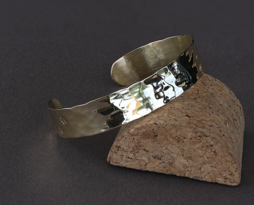Bracelet laiton martelé chat posé sur support en liège, reflet lumineux sur sa surface brillante.