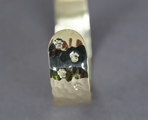 Gros plan sur le bracelet laiton martelé chat montrant cinq empreintes de pattes de chat poinçonnées sur le métal poli.