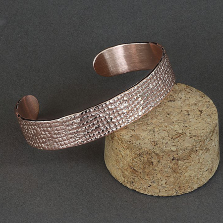 Bracelet ouvert en cuivre martelé à motif losange, présenté sur un support en liège