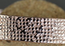 Gros plan sur le motif losange martelé d’un bracelet en cuivre artisanal, posé sur un support en liège.