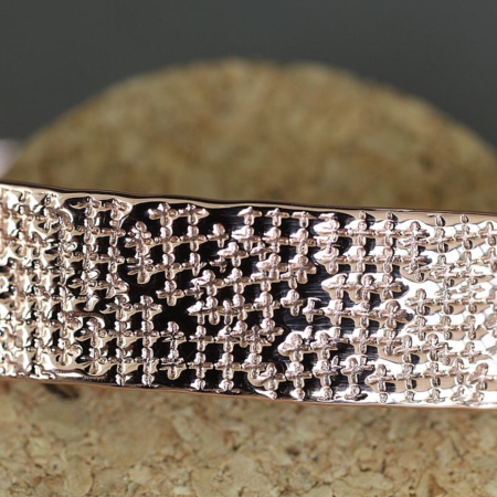 Gros plan sur le motif losange martelé d’un bracelet en cuivre artisanal, posé sur un support en liège.