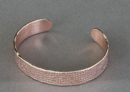 Vue de dessus d’un bracelet ouvert en cuivre martelé à motif losange, sur fond gris.