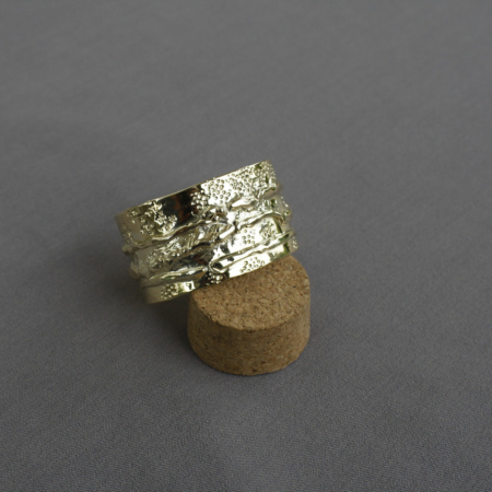 Bracelet en laiton martelé de style "destroy" au design brut et texturé, posé sur un support en liège.