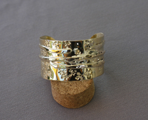 Bracelet en laiton martelé avec motifs en croix et surface déformée, posé sur un bouchon en liège.