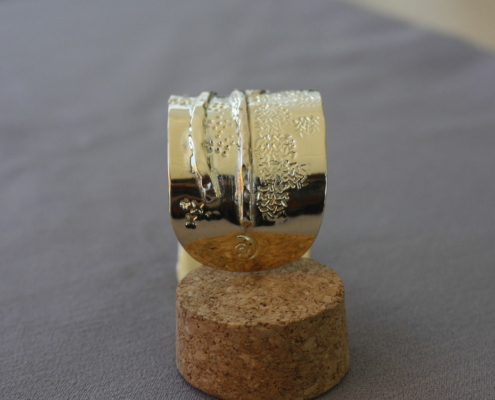 Bracelet en laiton martelé avec motifs en étoiles et reliefs asymétriques, présenté sur un socle en liège.