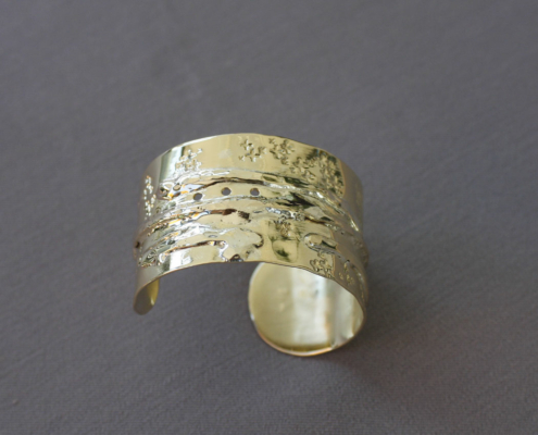 Bracelet en laiton martelé et texturé avec perforations alignées, reliefs organiques et finitions brillantes.