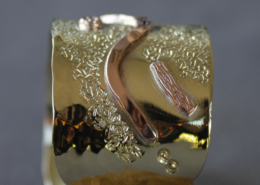 Bracelet large en laiton avec motifs en cuivre martelé, orné de formes ondulées et de rivets décoratifs.