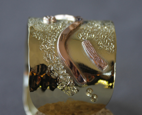 Bracelet large en laiton avec motifs en cuivre martelé, orné de formes ondulées et de rivets décoratifs.