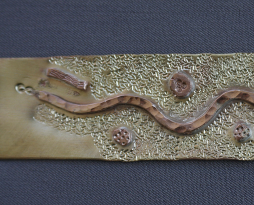Plaque de laiton brute en cours de fabrication d’un bracelet, décorée d’un motif ondulé en cuivre rouge martelé et de détails texturés.