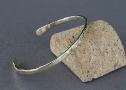 Bracelet fil en laiton martelé présenté en perspective sur un socle en liège, création artisanale Cuivre Island