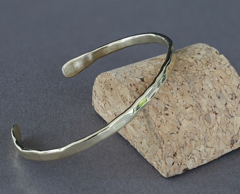 Bracelet fil en laiton martelé présenté en perspective sur un socle en liège, création artisanale Cuivre Island